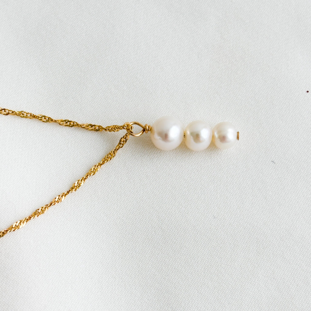 Gold Singapore chain necklace with a three graduated pearls pendant on a white background