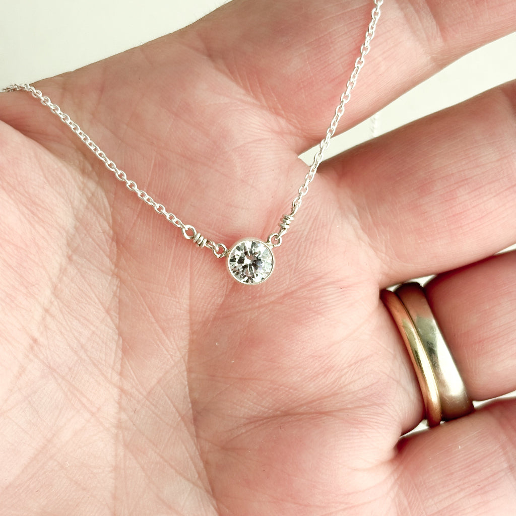 Silver necklace with a cz diamond solitaire pendant held in a hand.