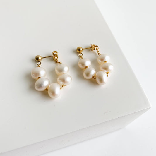 Baroque pearl earrings featuring 5 oval-shaped pearls strung on chain in a wrap around design to form a hoop that dangles from gold ball stud earrings.