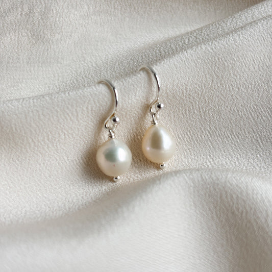 Plump pear shaped pearl on hook ear wire earrings on a soft white fabric background