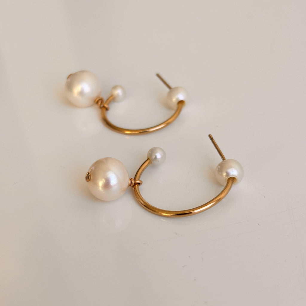 Gold hoop earrings with pearls on a light beige background