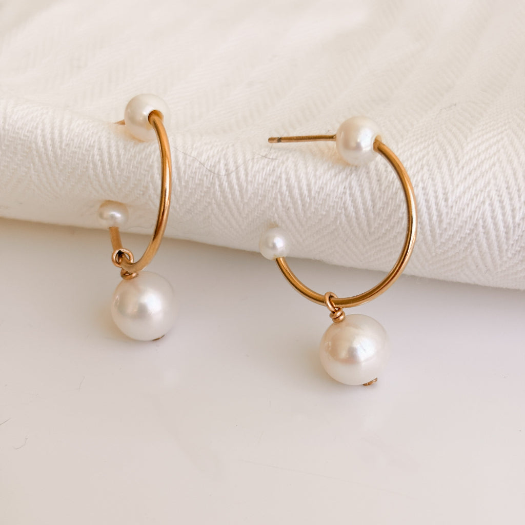 Gold hoop stud earrings with three pearls on a white surface