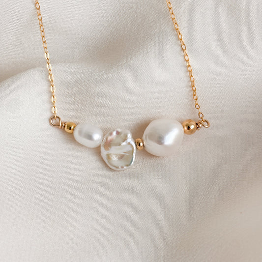 a dainty and unique gold pearl necklace featuring a trio of baroque pearls in different shapes; oval, biwa, and rice,  accented with petite gold beads and set into the chain.