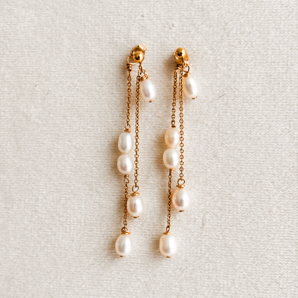 Pearl earrings with gold chains on a light gray background.  