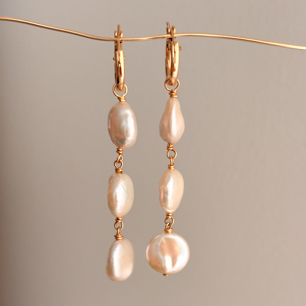 Pair of pearl earrings on a thin gold wire against a neutral background