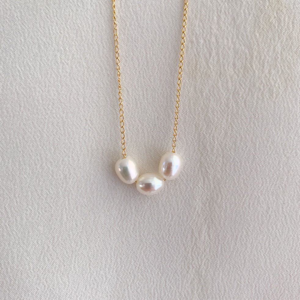 a dainty gold chain necklace featuring 3 petite oval pearls.