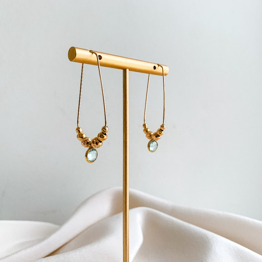 long teardrop hoop earrings featuring a bezel aquamarine charm and textured gold bead accents in 14k gold filled