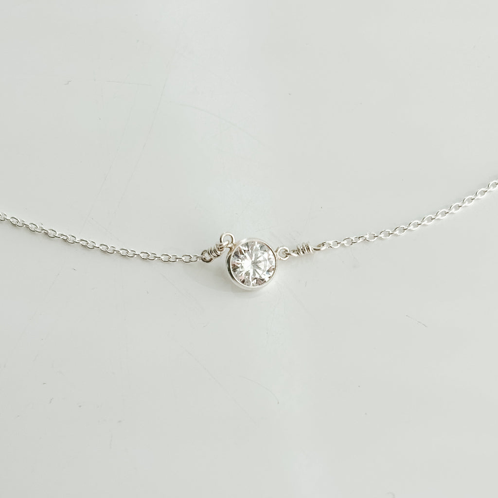 Delicate silver necklace with a small bezel set round cubic zirconia solitaire pendant on a light gray background