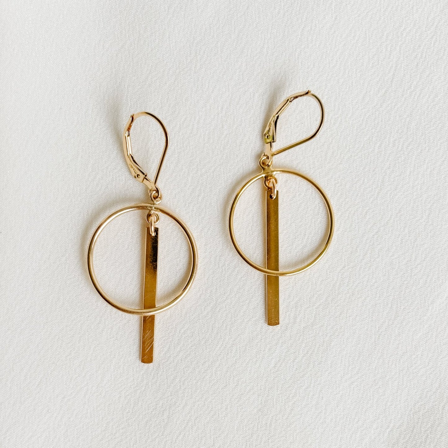 open circle frame earrings that feature a polished linear gold bar.  The circle and the bar dangle from lever back ear wires.