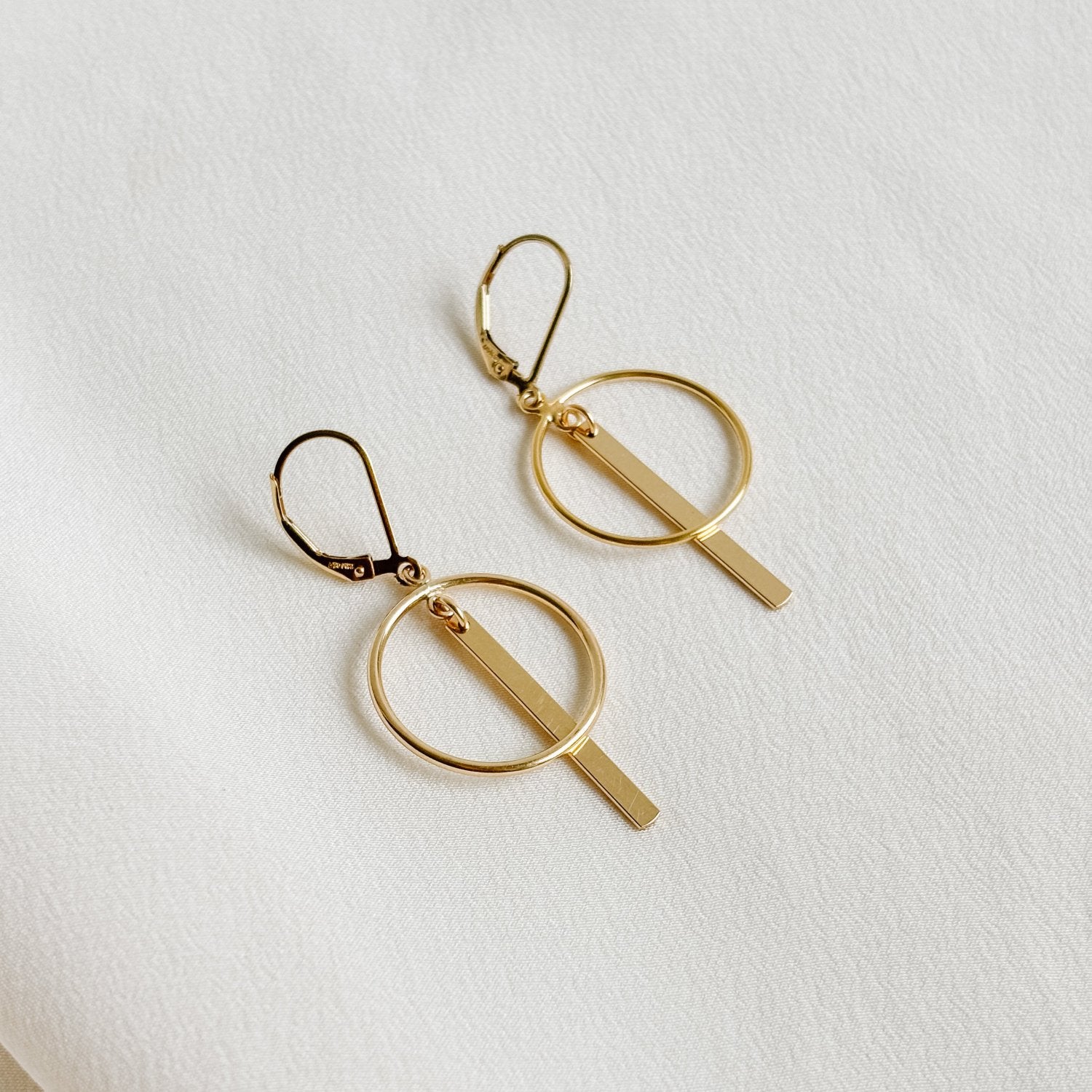 a pair of lever back earrings that feature an open circle frame and a linear gold bar.