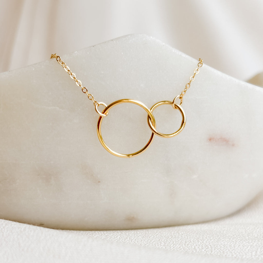 Gold necklace with interlocking rings on a marble surface
