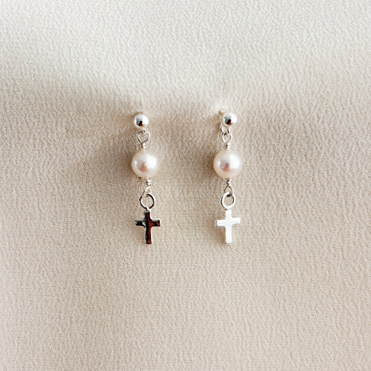 A pair of sterling silver ball post earrings with pearls and crosses on a beige background