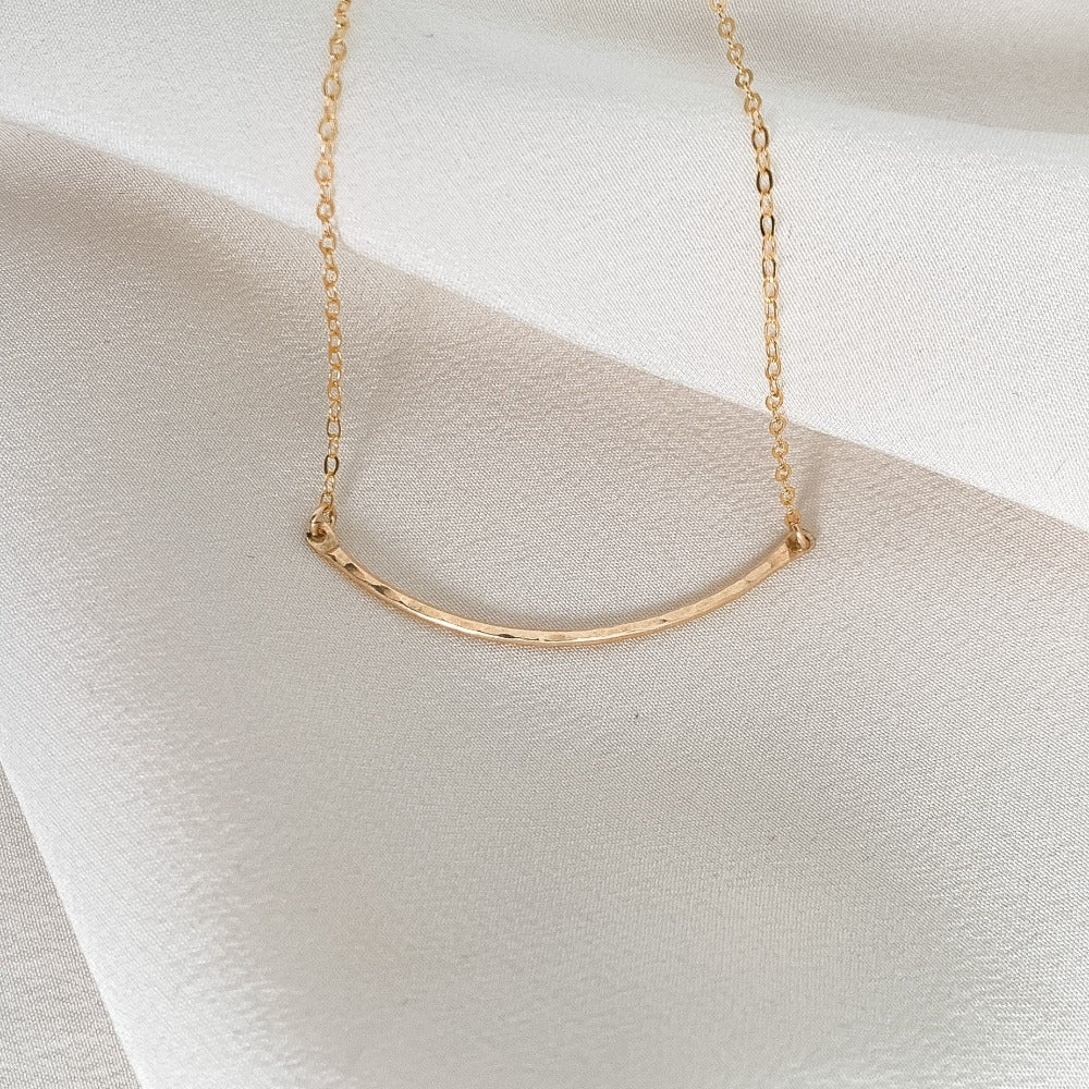 dainty gold necklace featuring a hammered curved bar set in the chain.