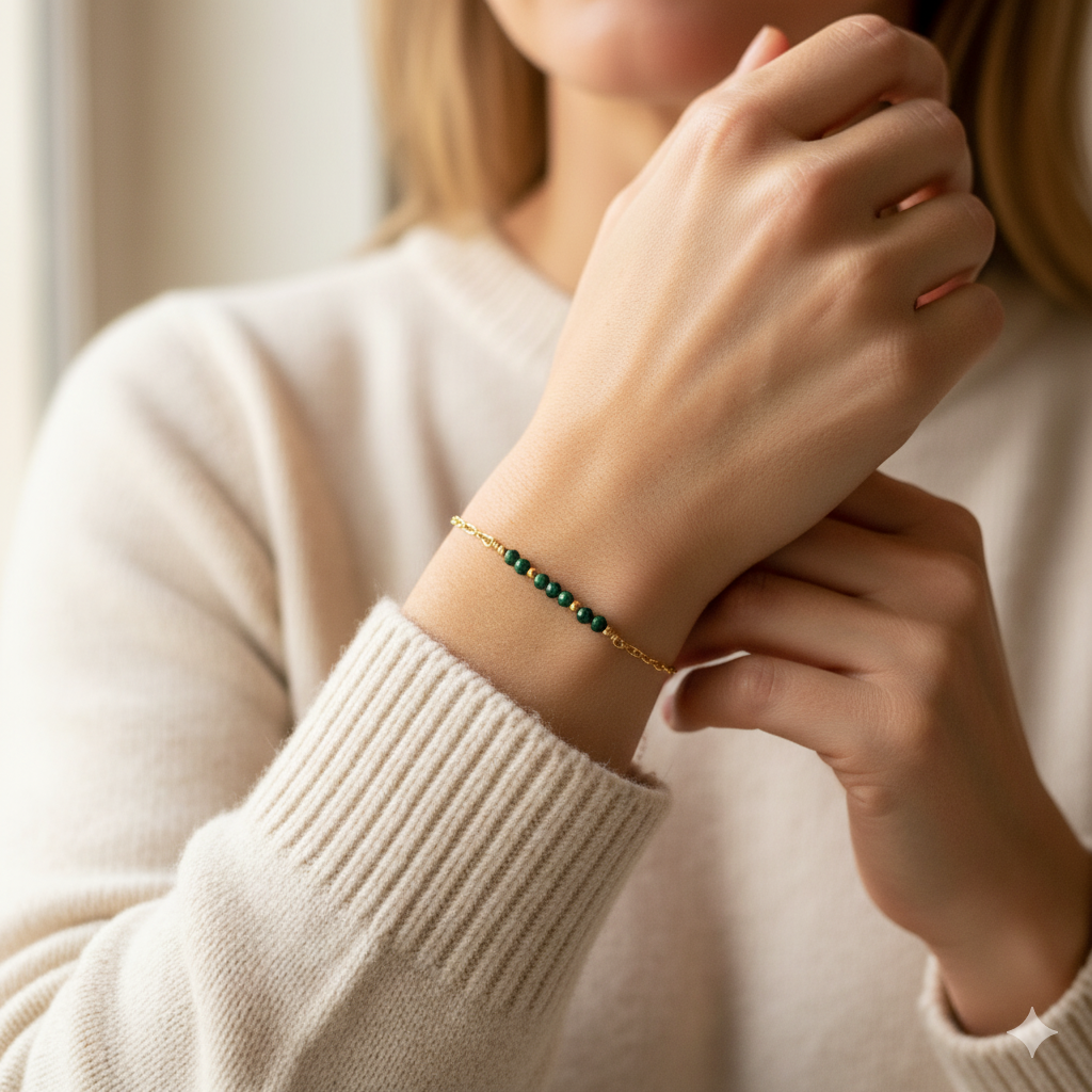 Close-up of a person wearing a green malachite bar and gold ball bead bracelet on a blurred background