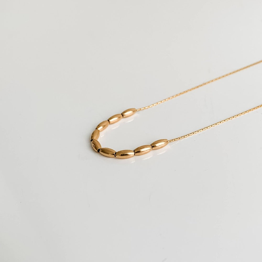 a gold pendant necklace showcasing 9 petite floating oval-shaped beads.