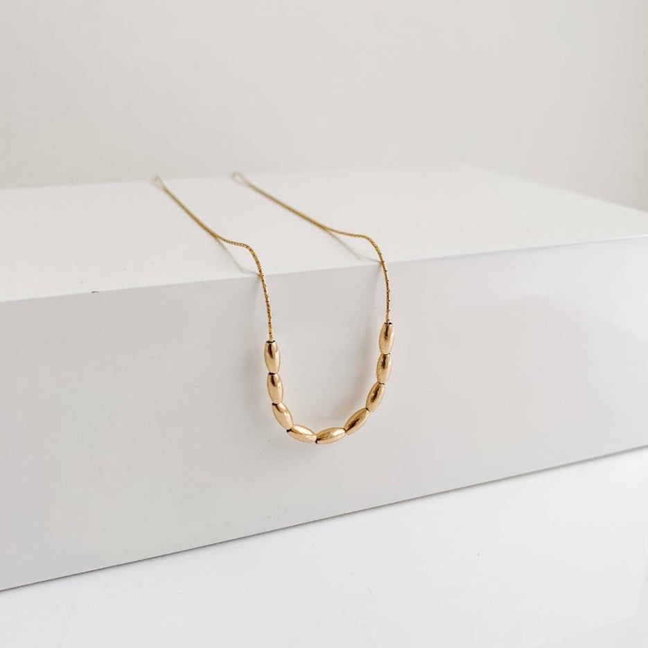 dainty gold necklace featuring 9 petite oval-shaped beads on delicate chain.