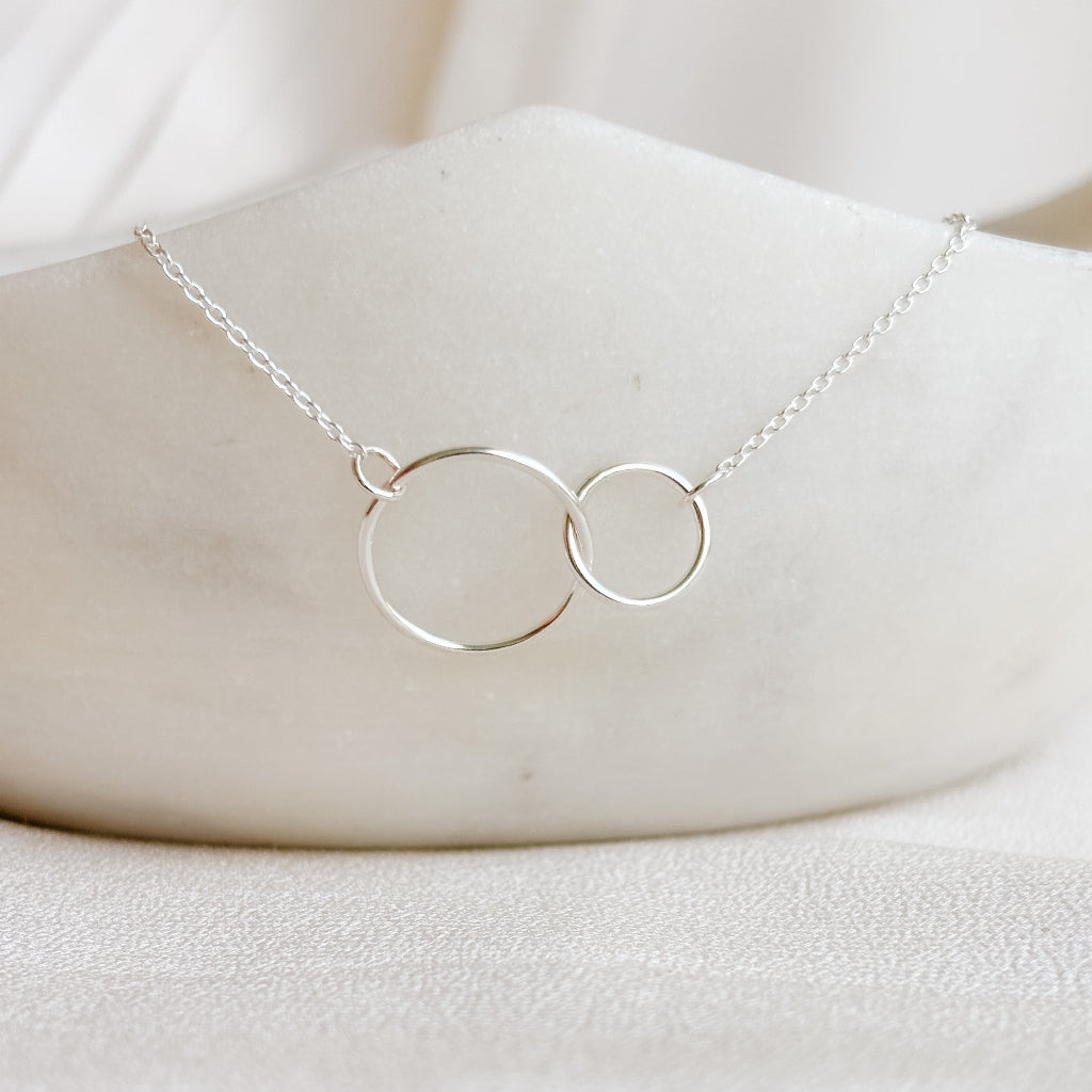 Silver necklace with two interlocking rings on a white marble surface