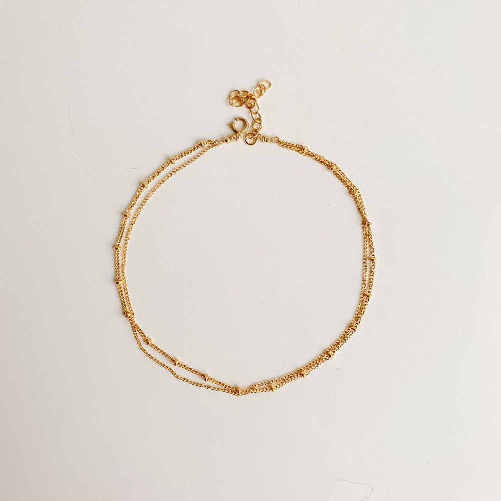 a dainty gold chain anklet featuring a beaded chain and a simple chain with spring ring closure. 