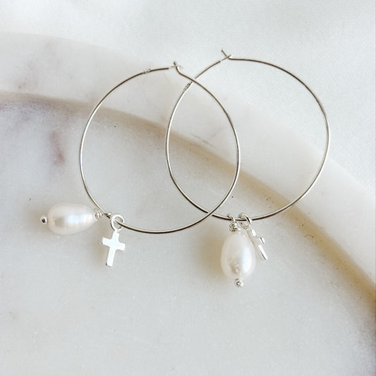 Silver hoop earrings with pearls and a cross on a light background