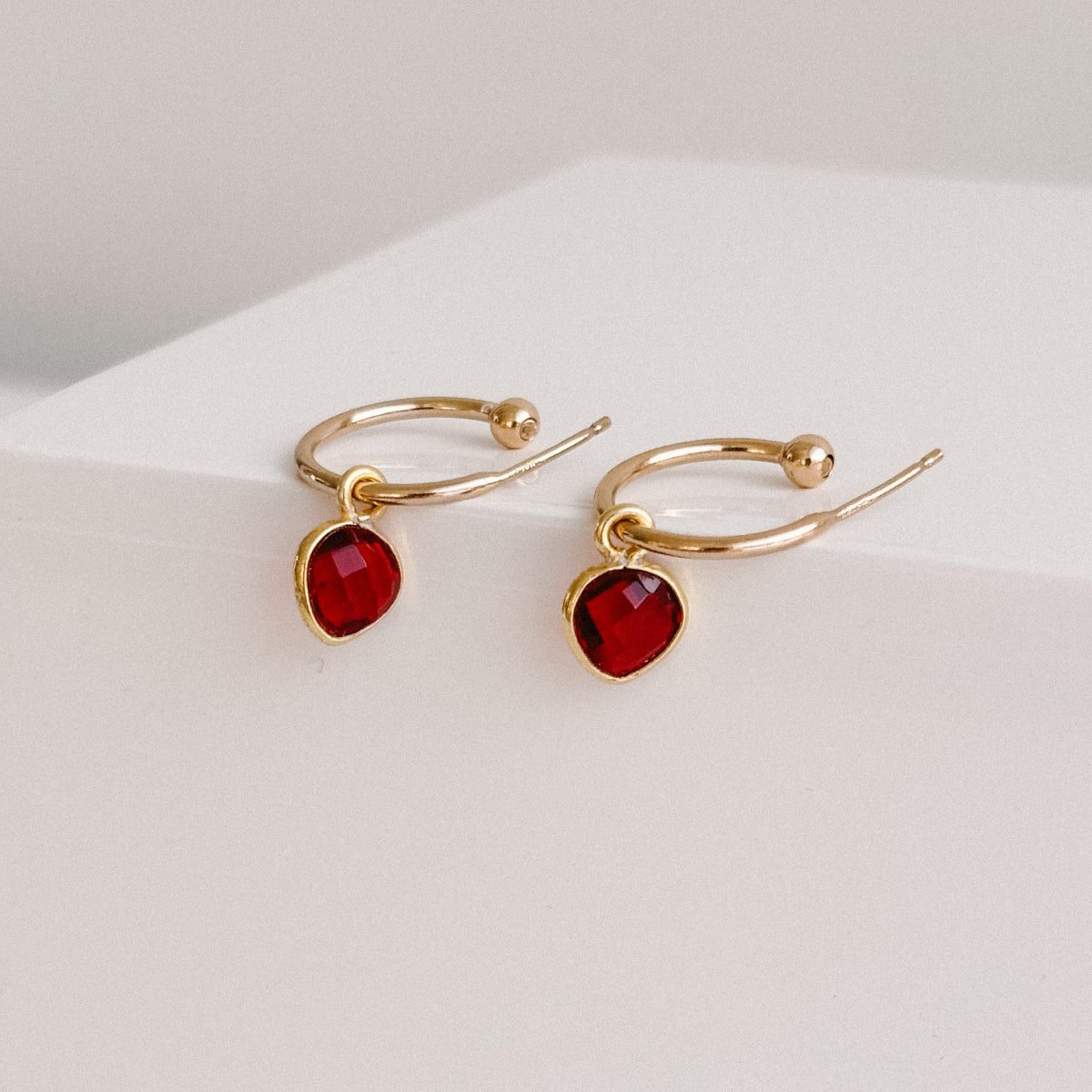 a pair of gold open hoop earrings with garnet heart charms