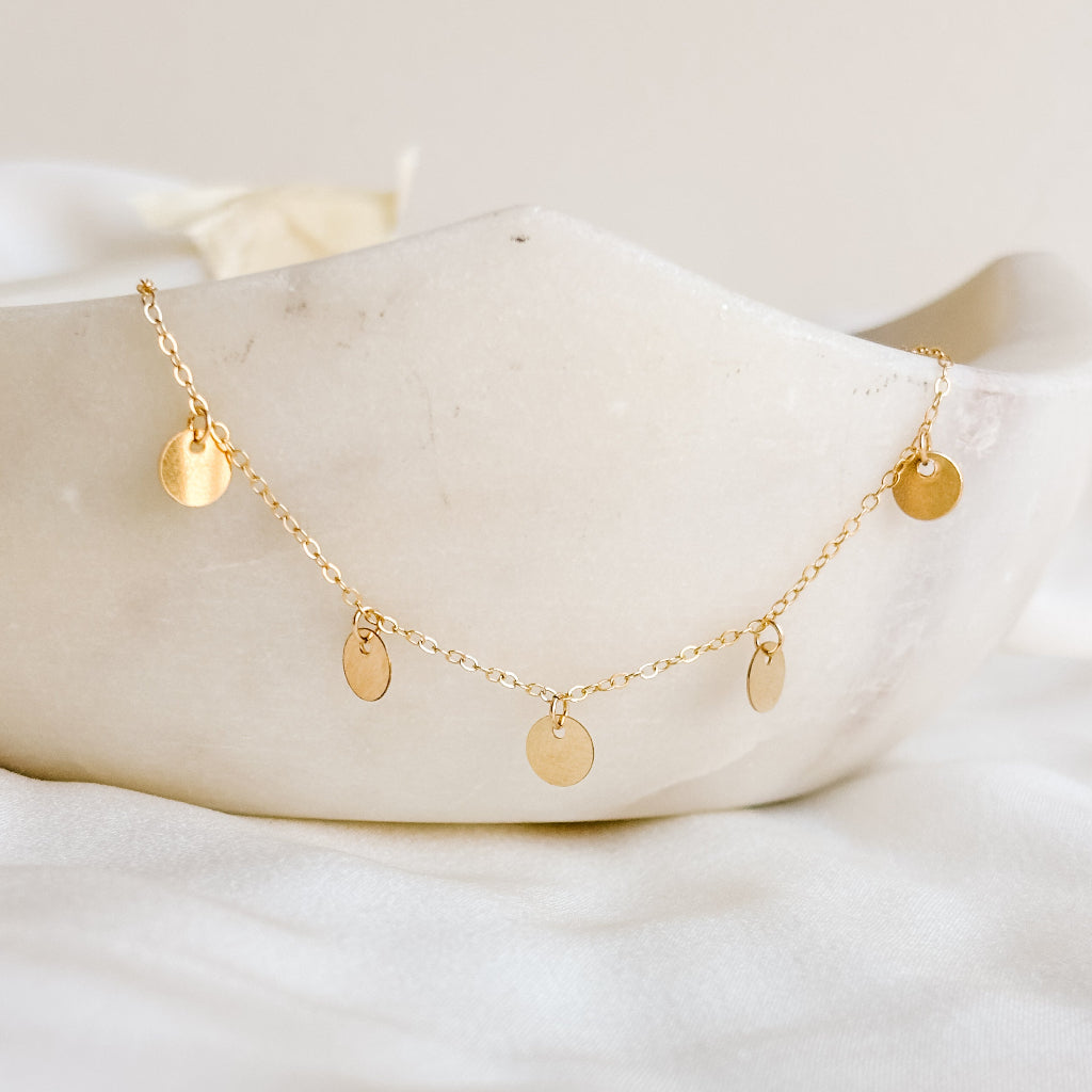 Gold necklace with 5 small  disc pendants on a white ceramic dish