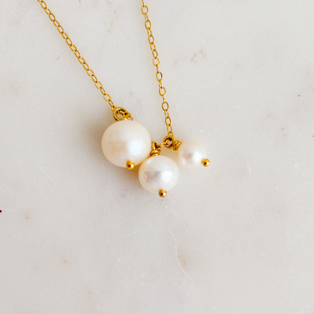 Gold necklace with three pearls on a light background
