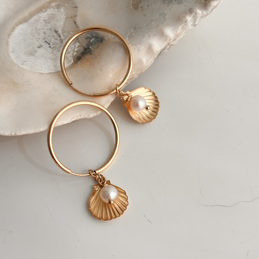 Gold hoop earrings with shell and pearl charms on a light background
