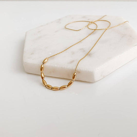 a dainty 14k gold filled necklace featuring 9 petite oval-shaped beads strung onto delicate chain.