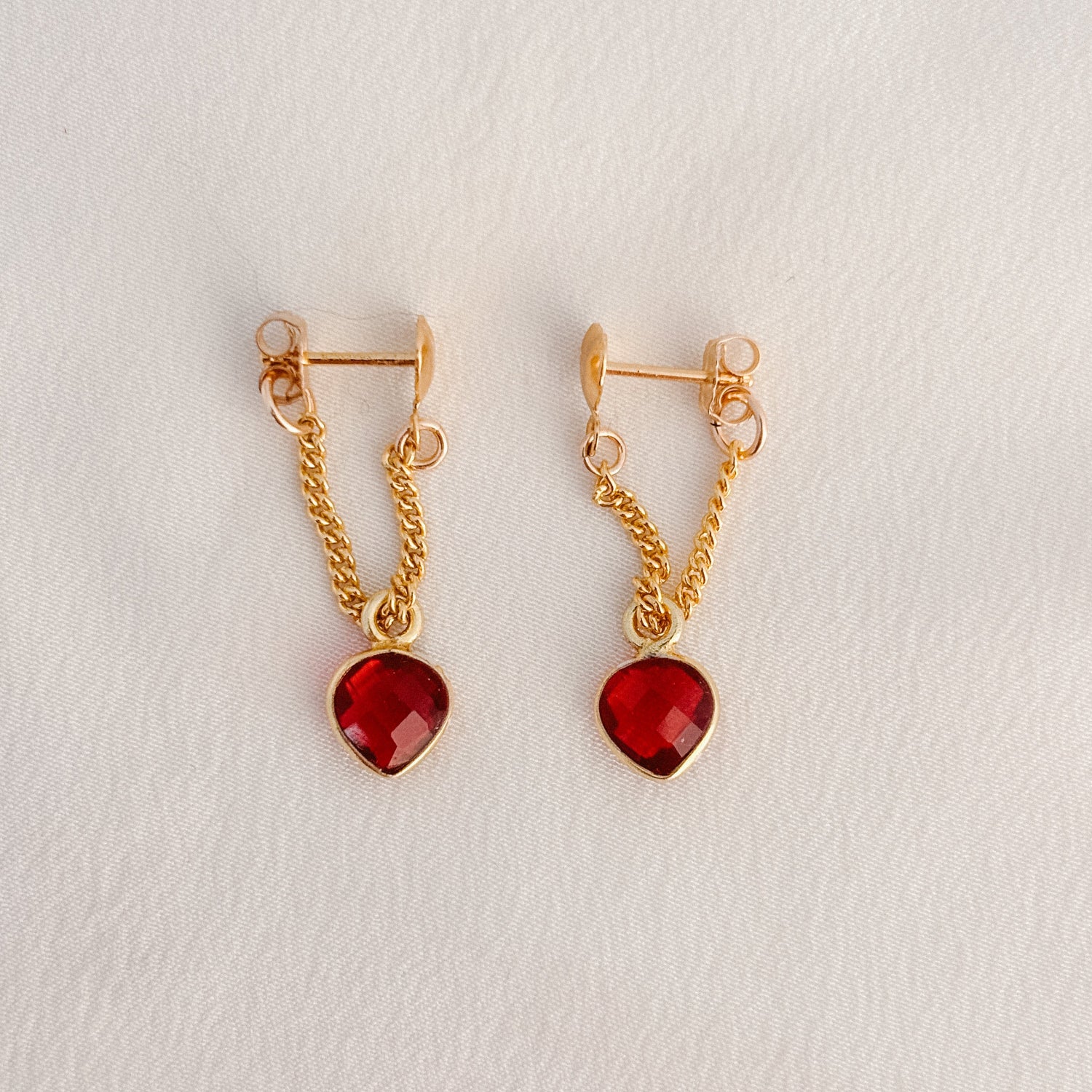 a pair of dainty 14k gold filled earrings that begin with petite heart shaped posts and feature faceted garnet heart shaped bezel set charms on curb chain.  The chain wraps around the lobe to form the hoop.  