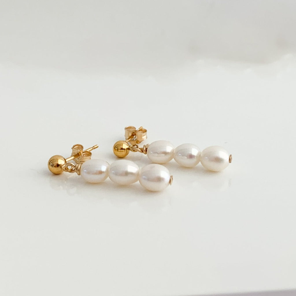a pair of dainty everyday pearl earrings featuring a stack of three petite oval pearls that dangle from gold ball stud earrings.