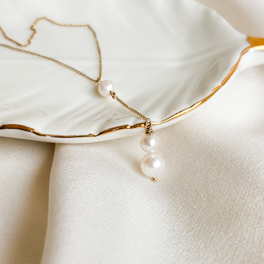 y shape Pearl necklace on a white dish with gold rim