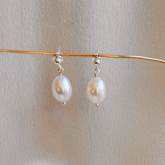 Oval pearl drop sterling silver ball post earrings on a thin gold wire against a light background.