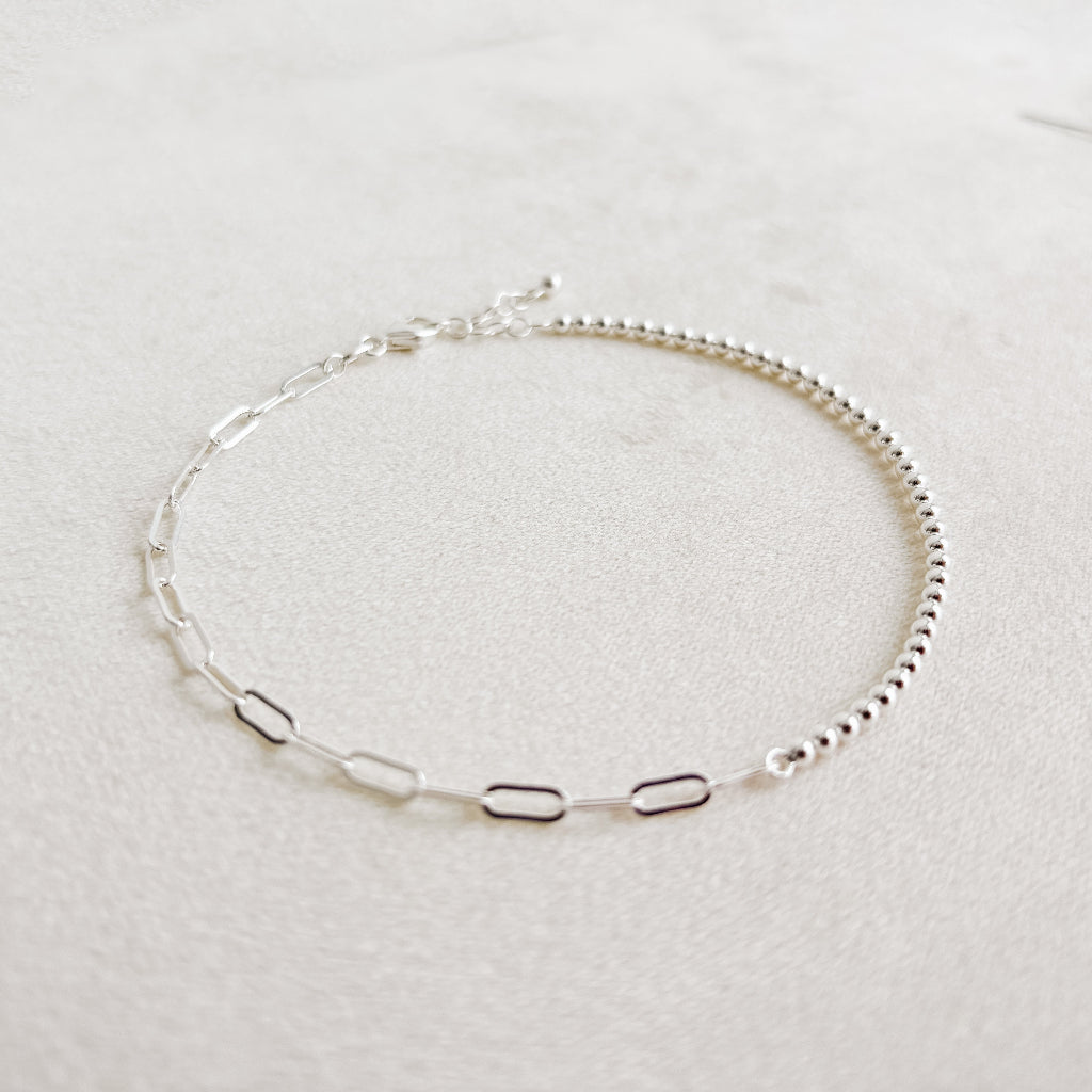 Silver beaded and paperclip ankle bracelet on a light gray background