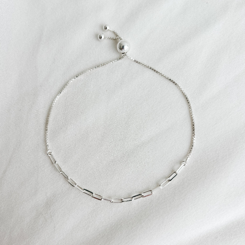 Silver paperclip anklet on a white fabric background