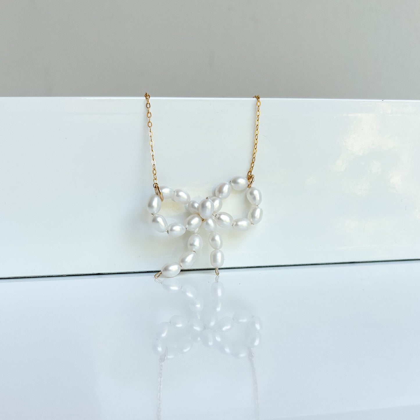 tiny oval beads form a bow pendant that is set in a fine cable chain necklace.  