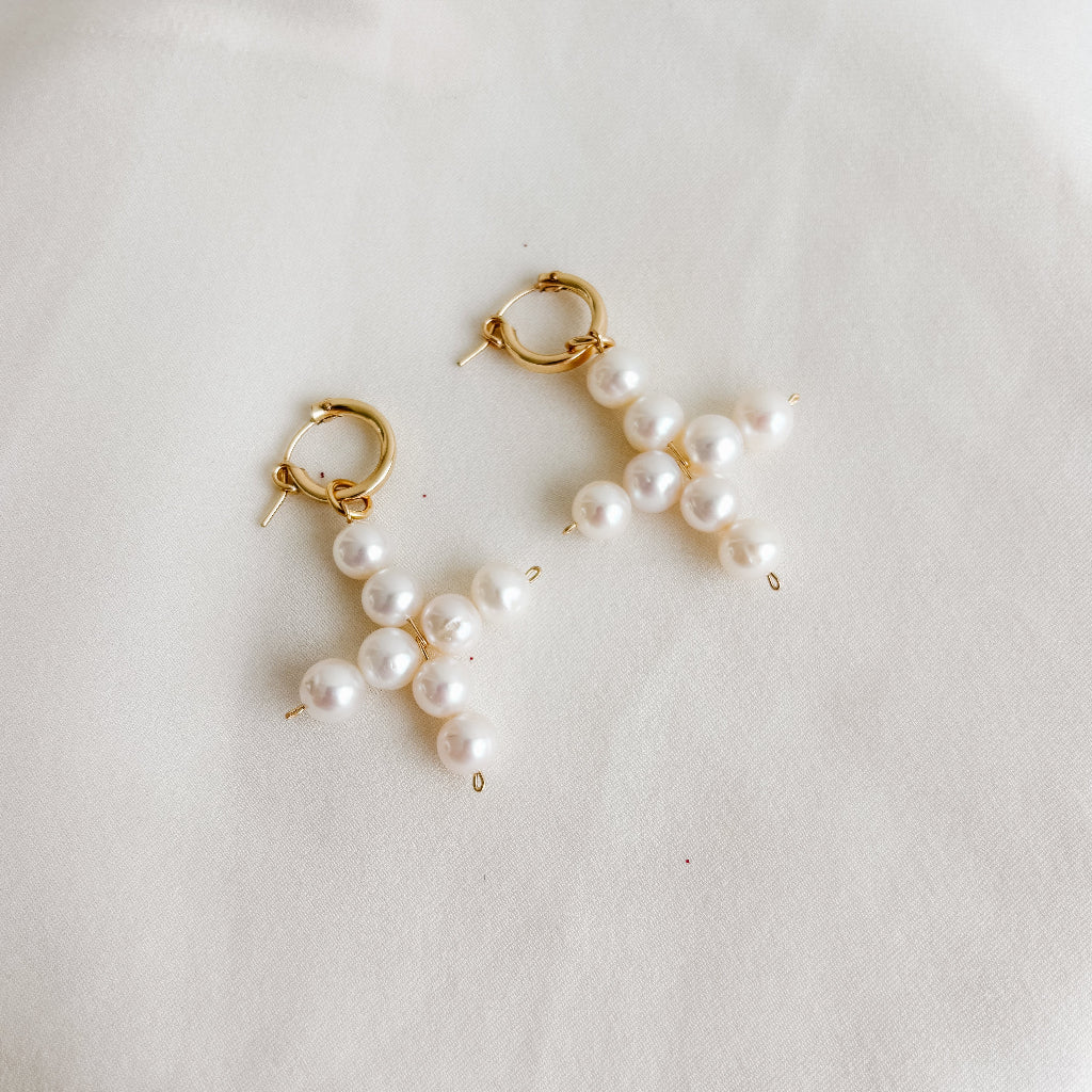 Pearl cross shaped charms on gold hoop earrings  on a light background