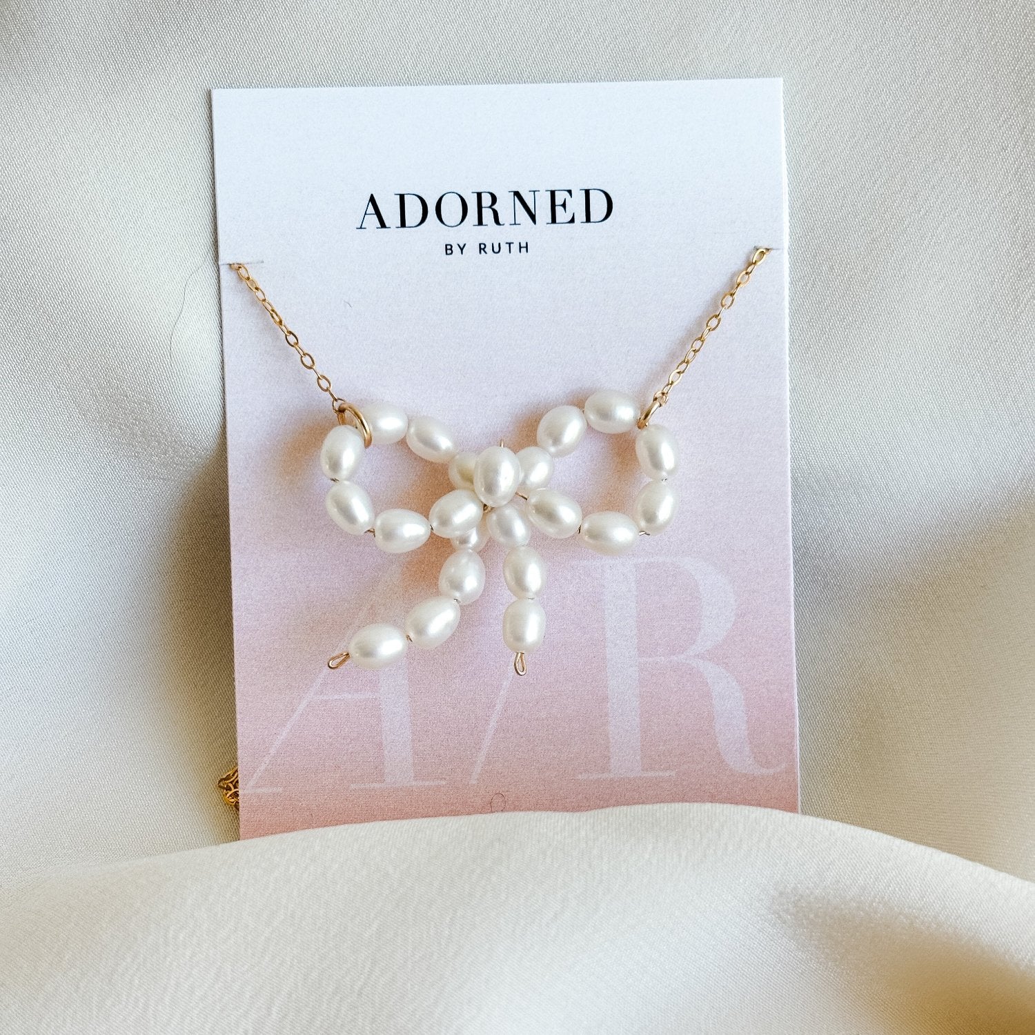 a dainty pearl bow pendant necklace shown on branded jewelry card.