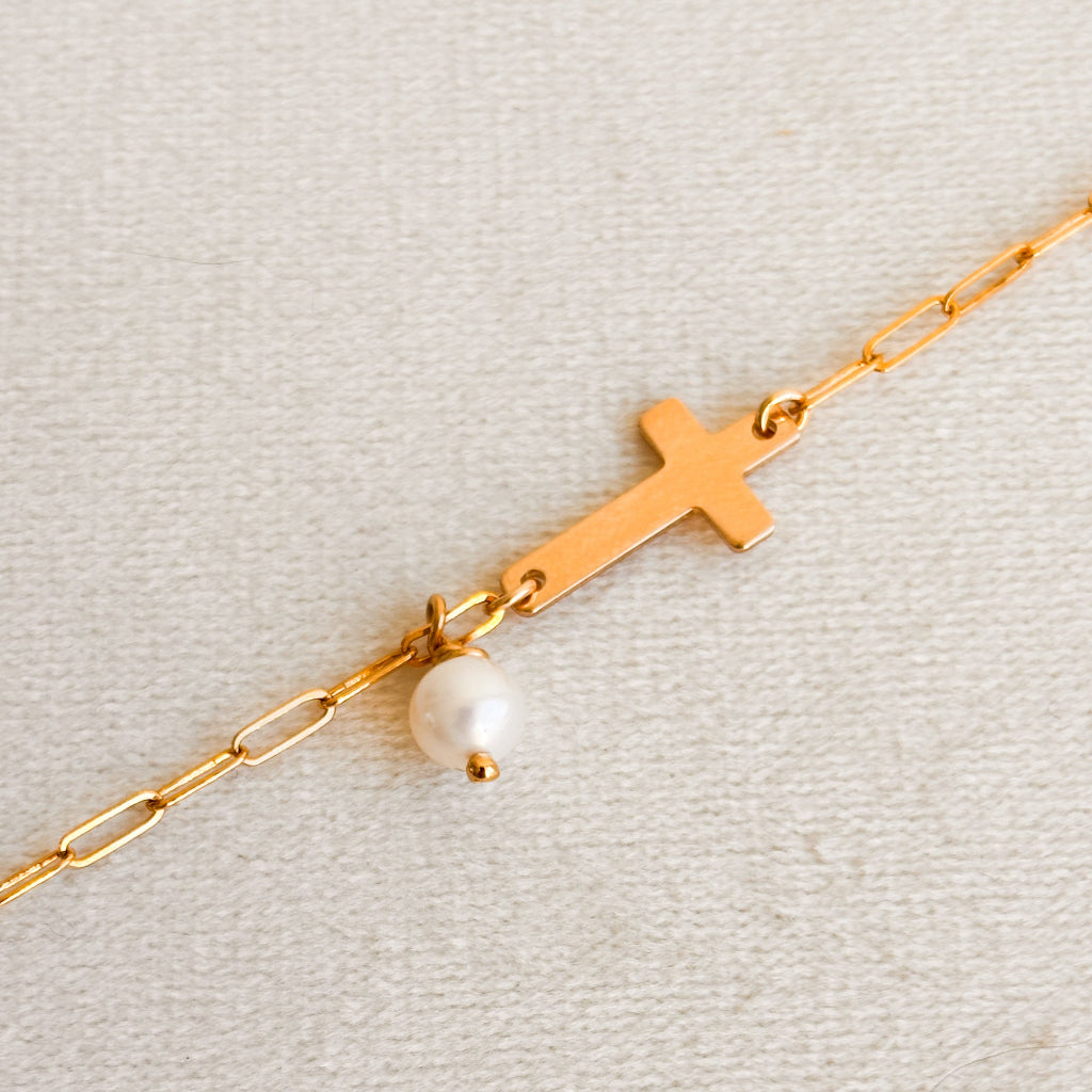 Gold bracelet with a cross and pearl on a light gray background