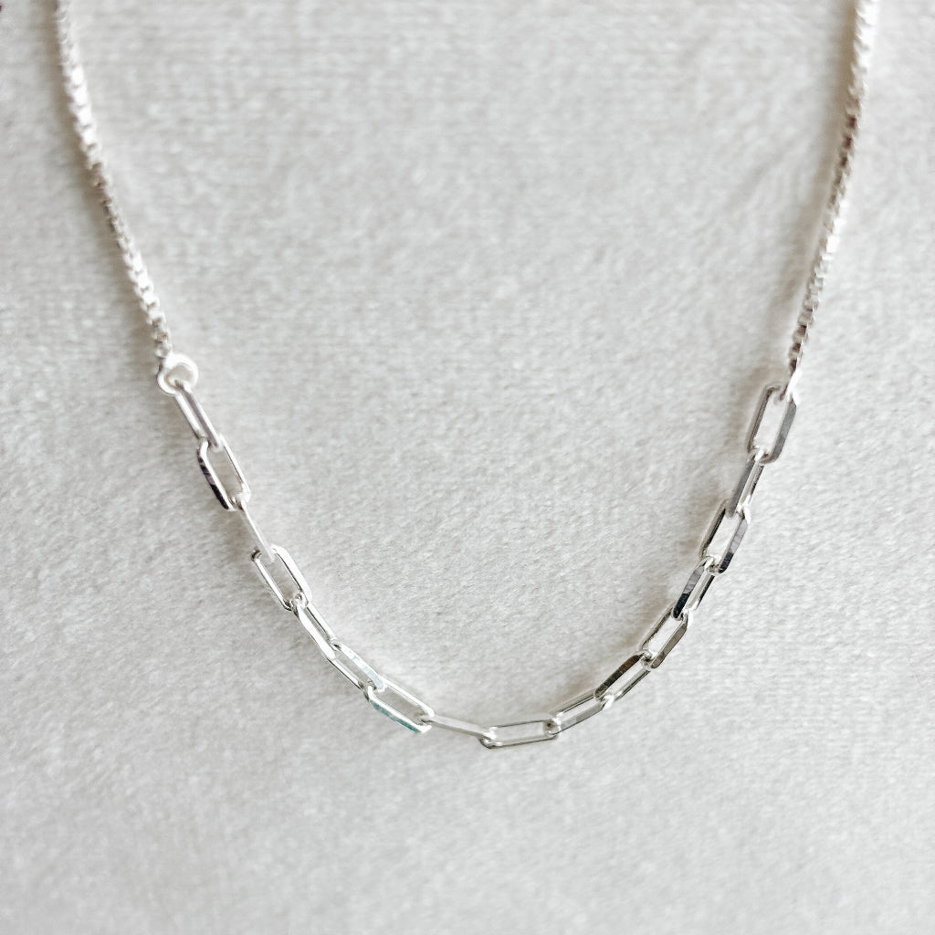 Silver paperclip and box chain ankle bracelet on a light gray background