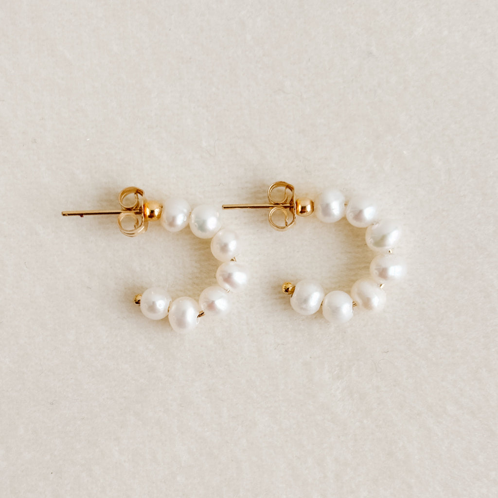Pair of pearl hoop earrings on a light beige background