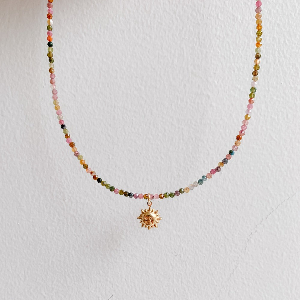 a dainty stone choker necklace crafted with tiny faceted watermelon tourmaline beads and featuring a smiling sunburst pendant in 14k gold filled. 