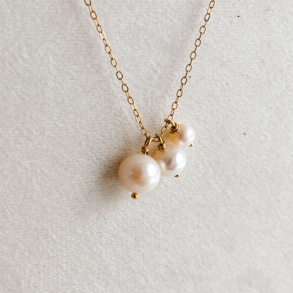 Gold necklace with three pearls on a light gray background