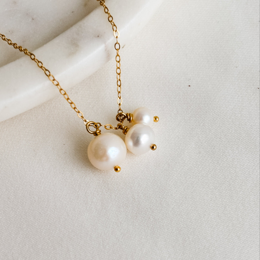 Gold necklace with three graduated pearls on a light background