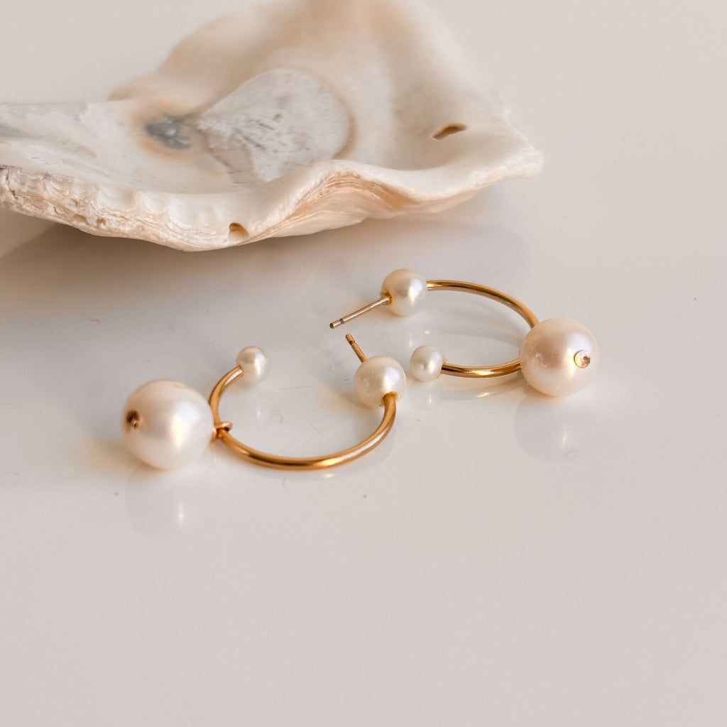 Gold open hoop earrings with pearls on a light background