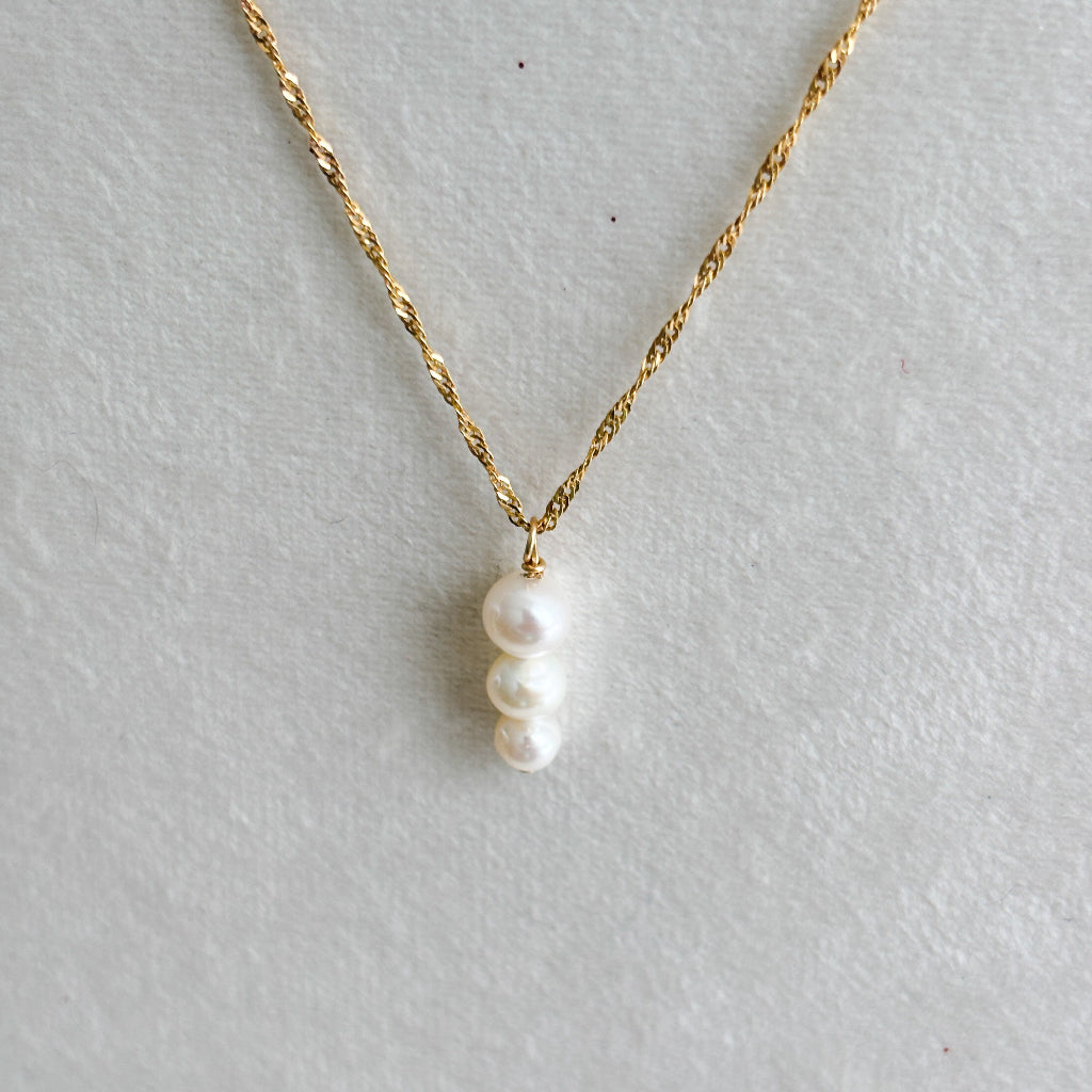 Gold necklace with a three-pearl pendant on a light gray background