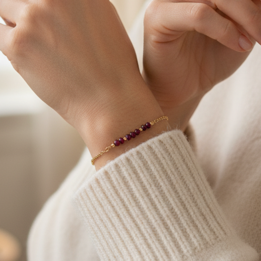 a dainty 14k gold filled Figaro chain bracelet with a row of tiny faceted garnet gemstones accented with gold ball beads set into the chain.