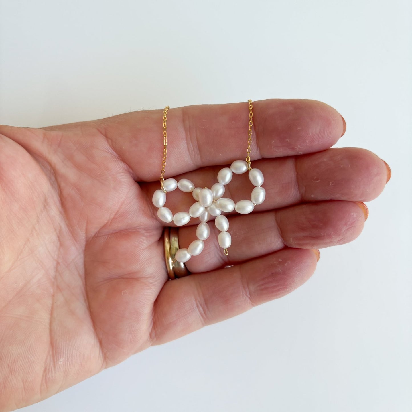 freshwater pearl bow pendant necklace shown in hand for size reference.