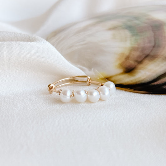 A dainty stacking pearl ring on a white surface with a shell in the background