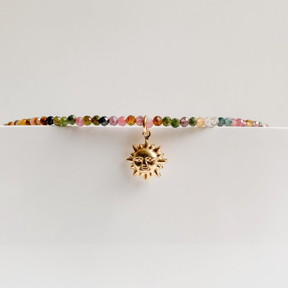 a dainty gemstone beaded necklace featuring a gold smiling sunburst pendant.