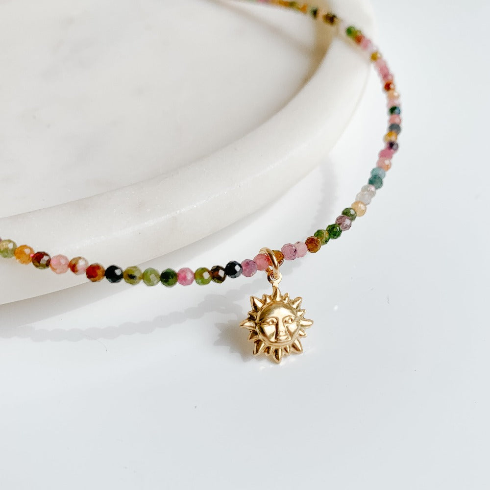 a dainty tourmaline beaded choker necklace featuring a gold sunburst charm pendant.